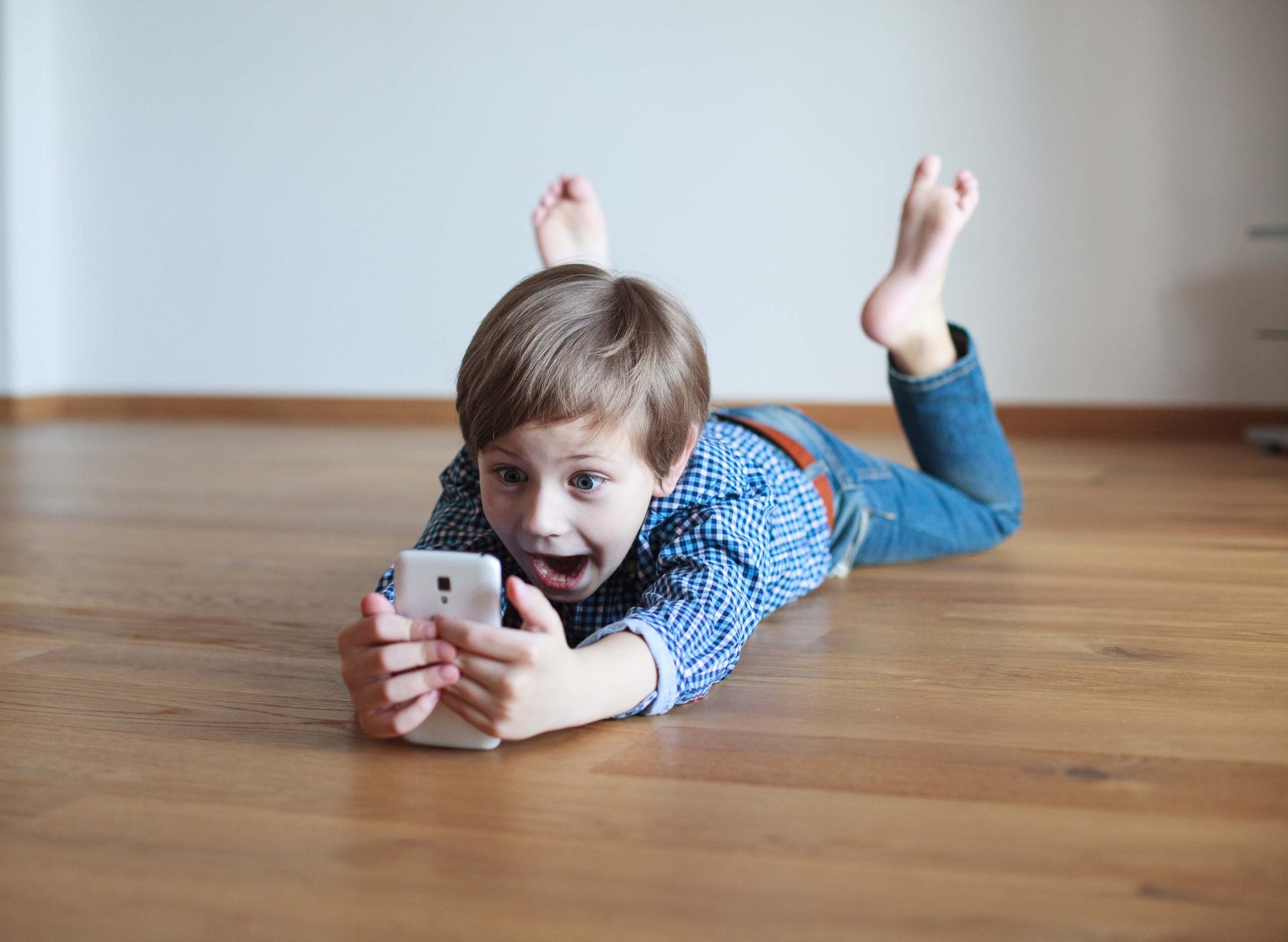 surprised boy lying on the wooden floor and using  mobile phone